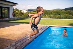 Two small children playing and jumping in swimming pool outdoors.