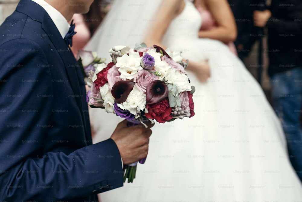 stylish groom and bride with rustic bouquet, posing in morning before wedding ceremony in church