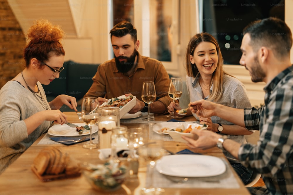 Young happy people communicating while having dinner together at dining table at home.