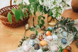Easter eggs on rustic background with basket, candle, spring flowers and green branches. Stylish colorful Easter eggs with modern ornaments painted with natural dye. Rural still life