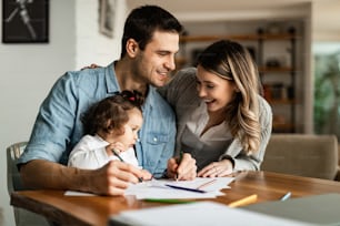 Young happy parents enjoying in coloring with their small daughter at home.