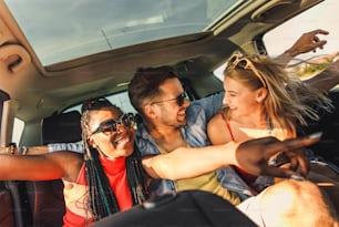 Three best friends enjoying traveling in the car, sitting in rear seat and having lots of fun on a road trip.