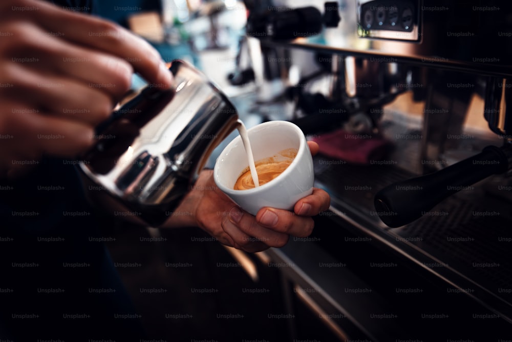 Gros plan sur les mains d’un barista préparant un cappuccino sur une machine à expresso pour un client dans un café.