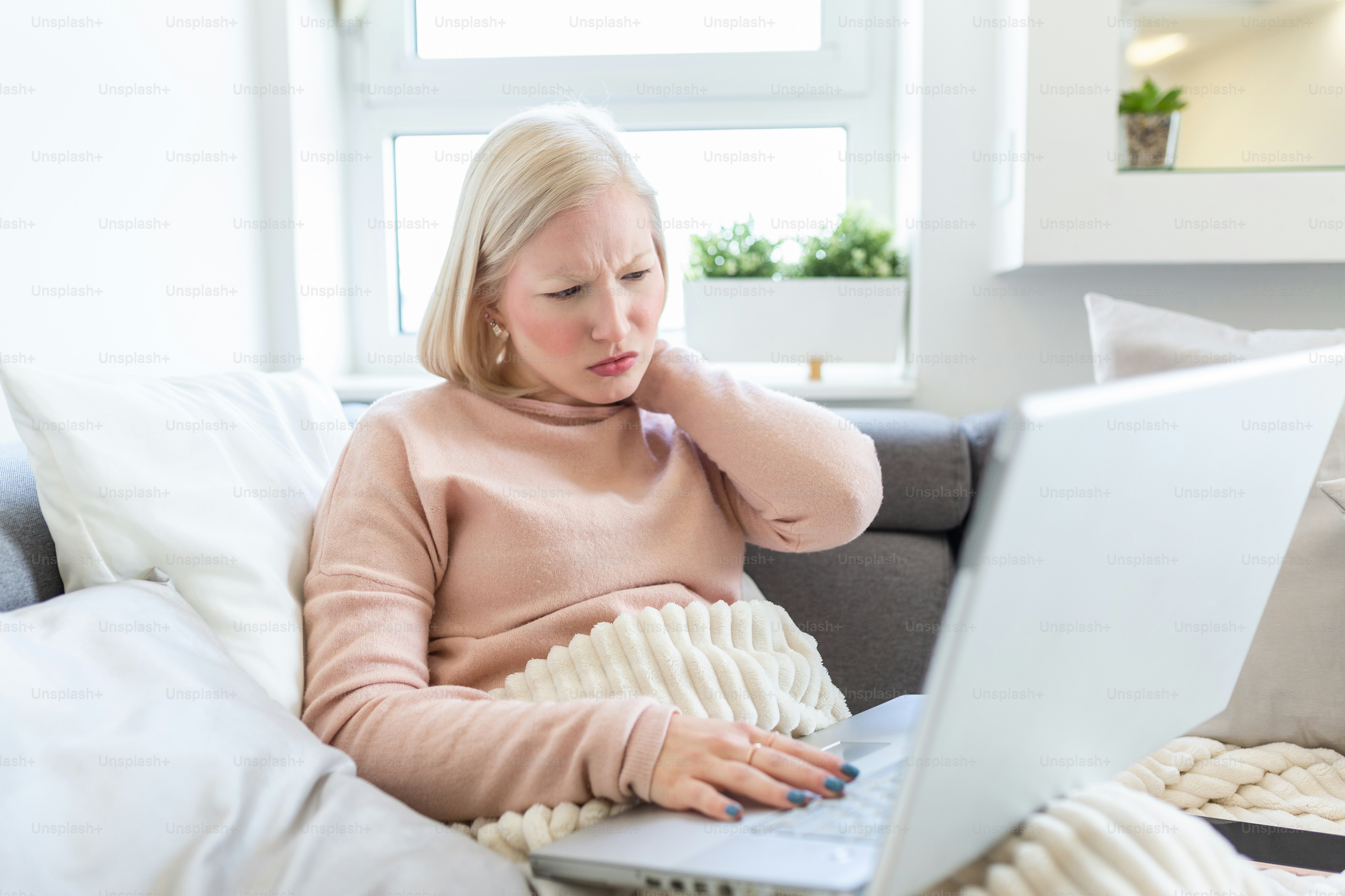 Feeling exhausted. Frustrated young woman looking exhausted and massaging her neck while working on her laptop. Tired Woman Massaging her Neck While Holding her Head.