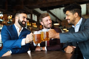 Velhos amigos alegres, homem de negócios se divertindo e bebendo cerveja no balcão do bar no pub.