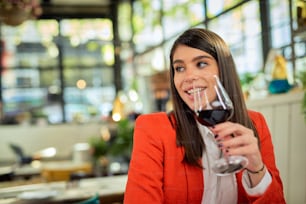 Smiling caucasian elegant businesswoman sitting in restaurant and holding glass of wine and enjoying lunch.