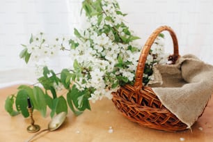 Stylish rustic basket with linen cloth and blooming cherry branches in soft light. Happy Easter concept. Eco friendly holiday. Rural still life