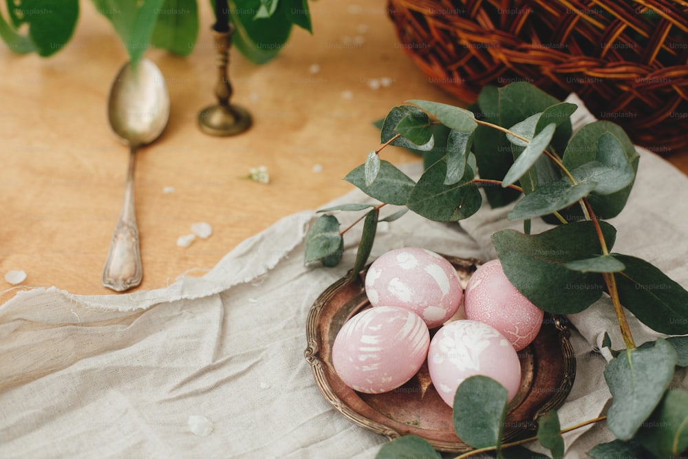 Modern Easter eggs with eucalyptus branch on rustic wooden table with basket and candle. Stylish pastel pink Easter eggs painted in natural dye from beets. Happy Easter