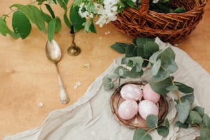 Oeufs de Pâques modernes avec branche d’eucalyptus sur table en bois rustique avec panier et bougie. Oeufs de Pâques rose pastel élégants peints en teinture naturelle à partir de betteraves. Joyeuses Pâques