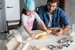 Padre e hija pequeña horneando pasteles. Familia divirtiéndose en la cocina y preparándose para una fiesta