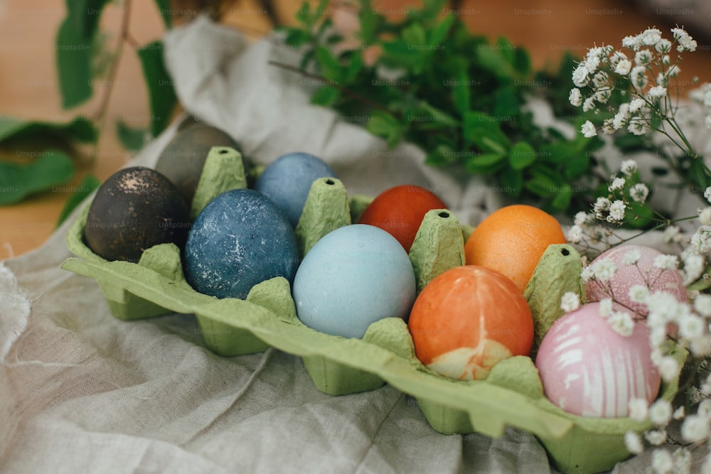 Natürliche Färbung Ostereier im Kartontablett auf rustikalem Tisch mit Blumen. Moderne gelbe, rosa, blaue und graue Ostereier bemalt mit Bio-Zwiebeln, Rüben, Rotkohl, Carcade-Tee. Zero Waste Urlaub