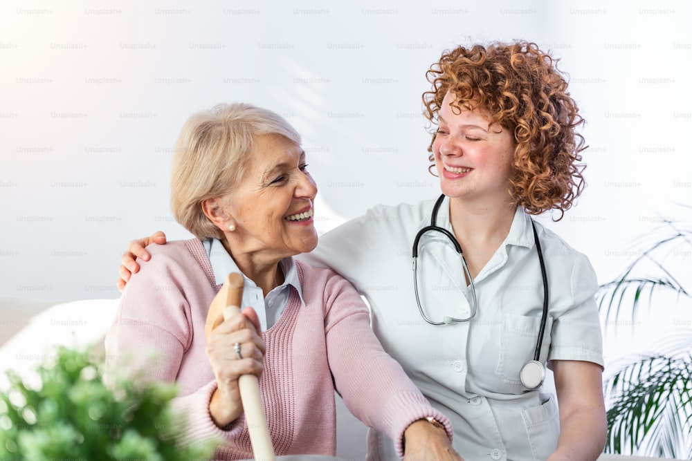 Friendly relationship between smiling caregiver in uniform and happy elderly woman. Supportive young nurse looking at senior woman. Young caring lovely caregiver and happy ward