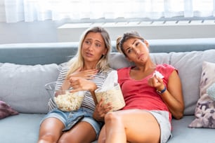 two best friends watch sad movie at home in bed crying touching. girls hold popcorn and tv remote control looking screen romantic film on television. ladies in pajama wiping tear using tissue