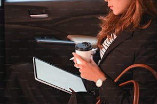 커피 컵과 스타일러스 펜을 손에 들고 편안한 차의 조수석에 앉아 있는 클로즈업 승객. 운송 중 작업의 개념.