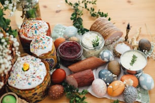 Easter modern eggs, easter cake, ham, beets, butter, cheese, sausages, green branches and flowers on rustic wooden table. Holiday preparation. Traditional Easter Food for breakfast