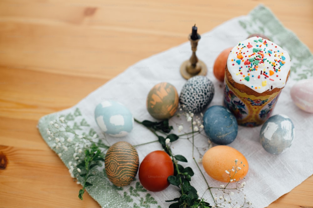 Homemade easter cake and stylish easter eggs natural dyed on rustic cloth with flowers and green brunches on wooden table. Happy Easter. Traditional Easter food. Copy space
