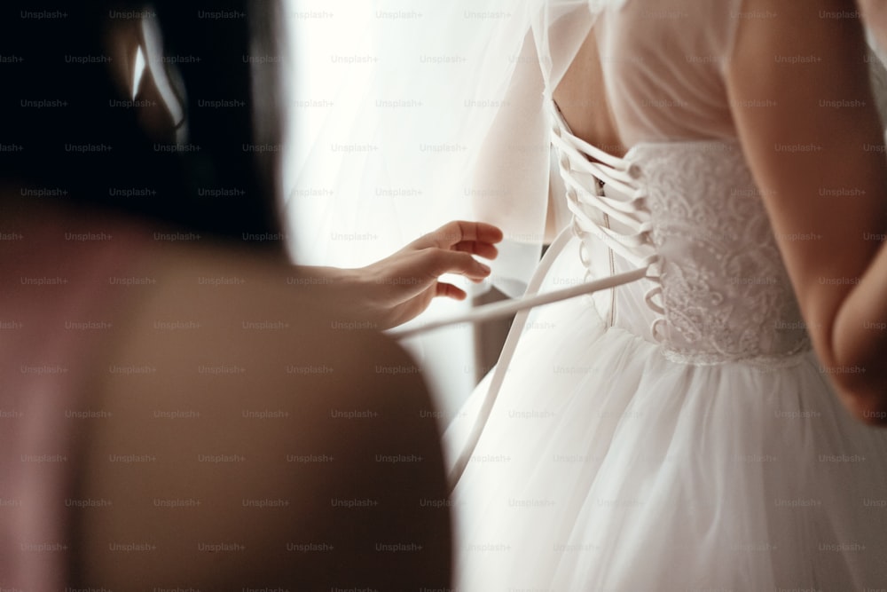 Les demoiselles d’honneur aident la mariée à s’habiller en robe de mariée, à se préparer et à se préparer le matin pour la cérémonie de mariage.