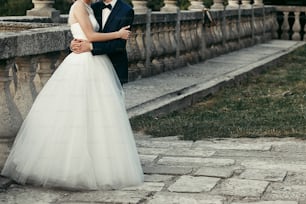 wedding couple hugging on background of old castle. elegant bride and groom gently embracing. man in classic suit with bow tie and woman in white dress with pearls. space for text.