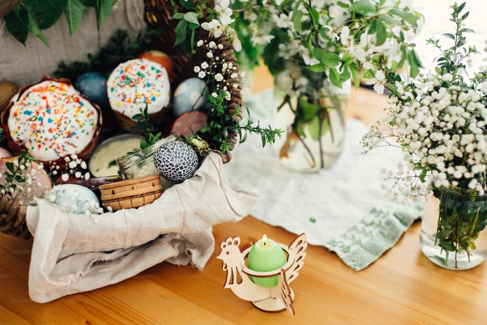 教会での祝福のための伝統的なイースターバスケット。イースターモダンの卵、ケーキ、ハム、ビート、素朴なバスケットのバターは、キャンドルと木製のテーブルの上に緑のbuxusの枝や花で飾られています