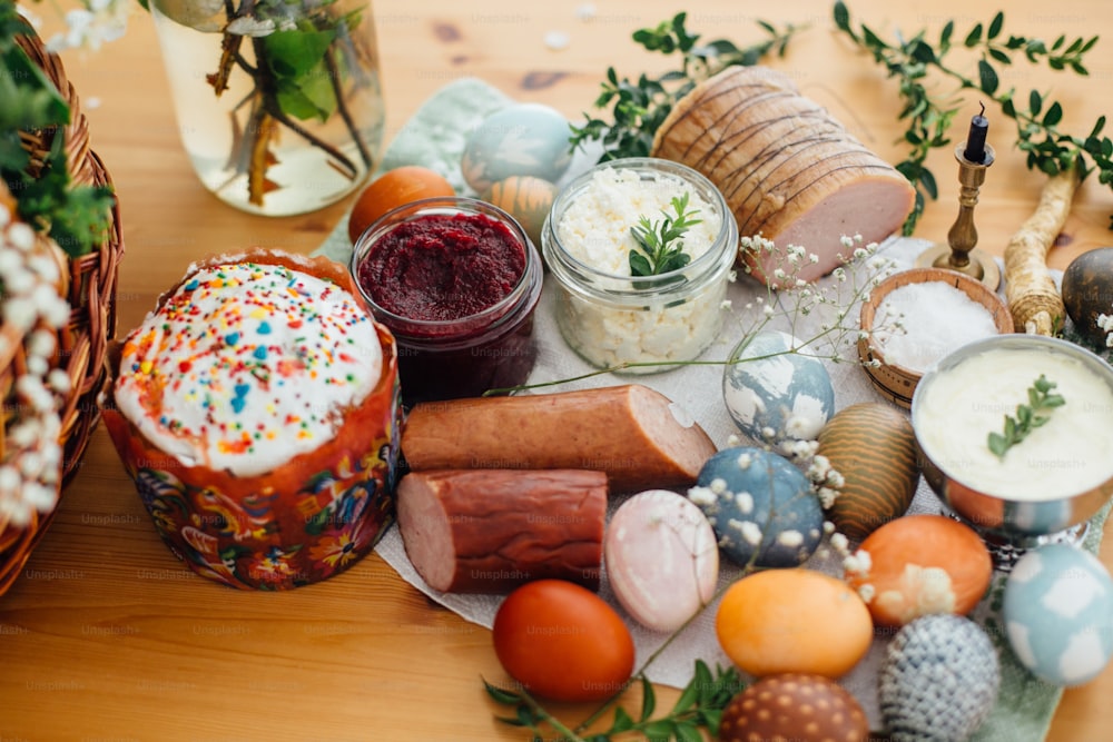 Traditional Easter Food. Easter modern eggs, easter bread, ham, beets, butter, cheese, sausages, green branches and flowers on rustic wooden table. Holiday preparation. Easter brunch