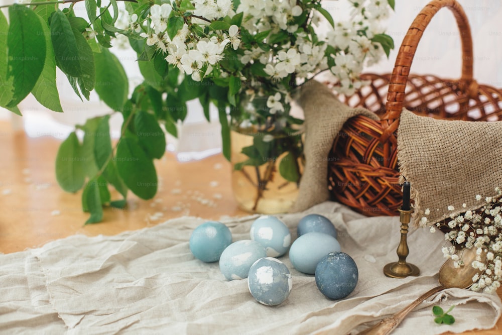 Oeufs de Pâques modernes sur table rustique avec des fleurs de printemps, panier, toile de lin. Élégants œufs de Pâques bleu pastel peints dans une teinture naturelle à partir de chou rouge. Joyeuses Pâques. Nature morte rurale