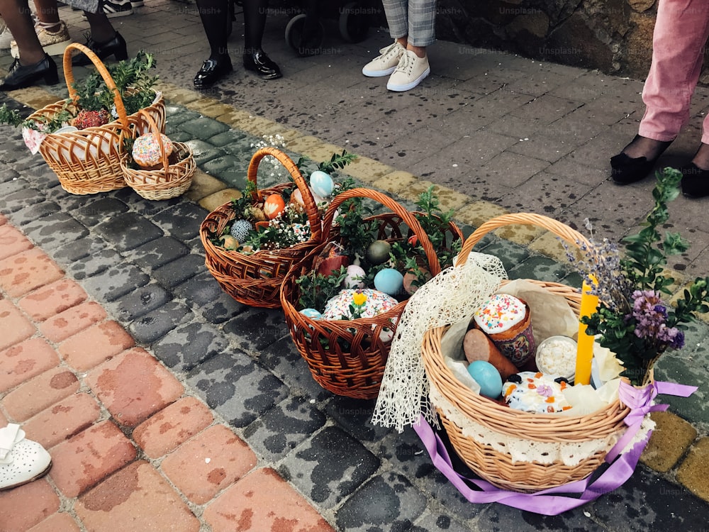 Easter baskets with stylish painted eggs, easter cake, ham,beets, butter, candle with boxwood branches for sanctify at church on background of people feet. Easter food for blessing