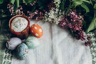 happy easter. easter cake and colorful decorated eggs on rustic background with lilac flowers.  egg with floral and chicken ornaments. space for text.  greeting card concept. top view