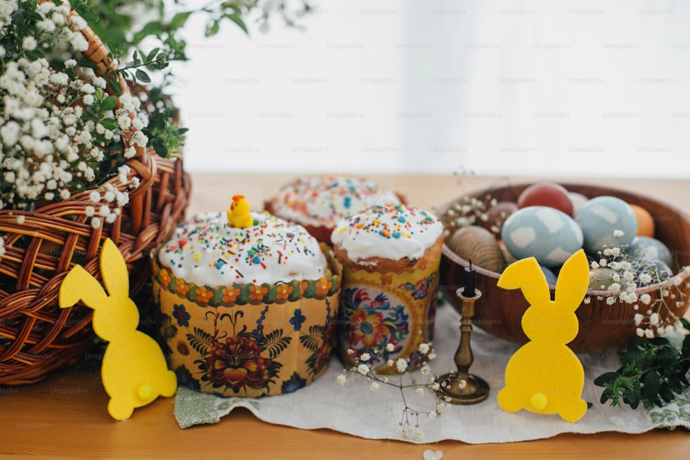 Homemade easter cake, stylish easter eggs natural dyed, candle, bunny decor, green branches and flowers on wooden background. Easter Food for sanctify. Happy holiday