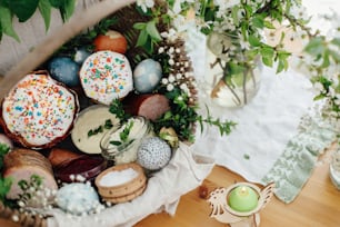 Traditional Easter basket for blessings in church. Easter modern eggs, cake, ham, beets, butter in rustic basket decorated with green buxus branches and flowers on wooden table with candle