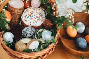 부활절 현대 계란, 부활절 빵, 햄, 사탕무, 버터, 소박한 나무 테이블에 녹색 buxus 가지와 꽃으로 장식 된 고리 버들 바구니에. 전통적인 부활절 바구니.