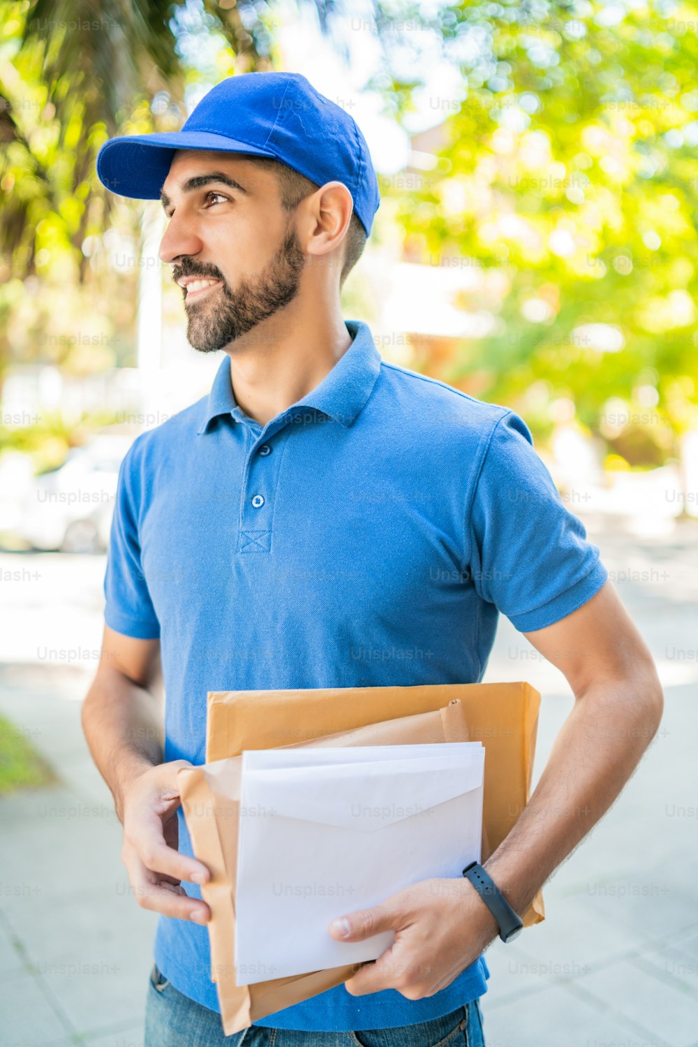 Close-up of a postman carrying packages and letters outdoors in the street. Delivery postal service concept.
