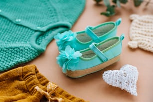 Close up of baby girl mint shoes on beige background near clothes and heart.
