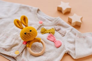 Close up of wooden knitted bunny beanbag teether on baby girl clothing on beige background.