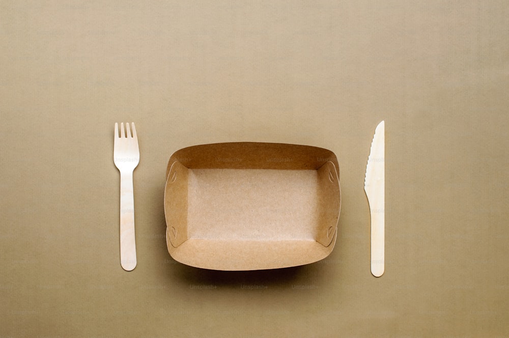 Disposable eco friendly food packaging. Brown kraft paper food container on beige background. Top view, flat lay.