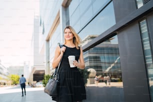 Retrato de una joven mujer de negocios que camina hacia el trabajo mientras bebe café para llevar. Concepto de negocio y éxito.