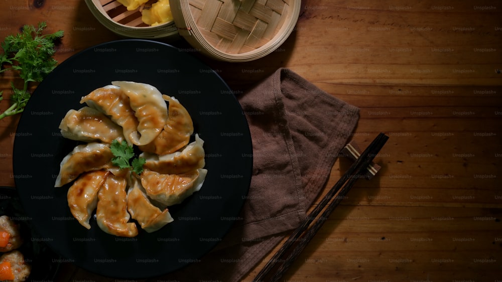 Top view of Dim sum with fried Japanese Gyoza dumplings on black plate and Chinese dumplings served on traditional steamer