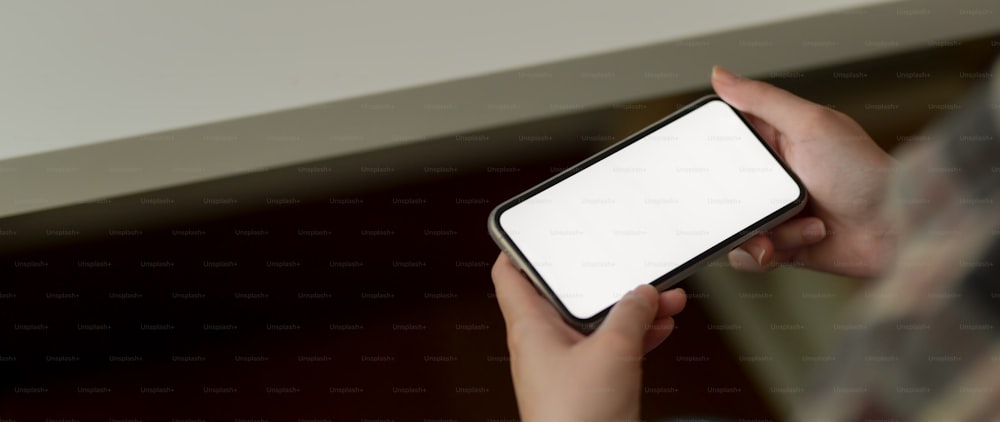 Cropped shot of female holding horizontal mock-up smartphone while sitting at minimal workspace