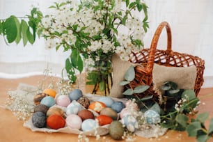 Happy Easter. Easter eggs on rustic background with basket, spring flowers and green branches, rural still life. Stylish colorful Easter eggs with modern ornaments painted with natural dye