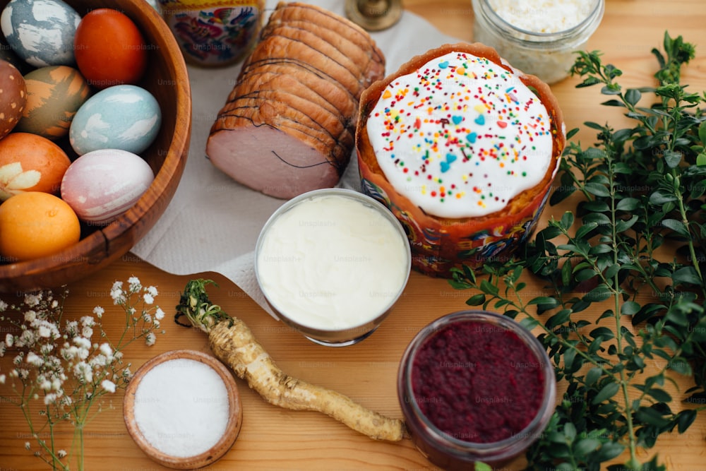 イースターモダンエッグ、イースターケーキ、ハム、ビート、バター、緑の枝、花を籐のバスケット用の素朴な木製のテーブルに。休日の準備。伝統的なイースターフード