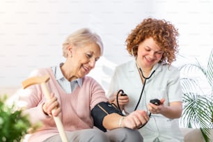 Caregiver che misura la pressione sanguigna di una donna anziana a casa. Gentile badante che misura la pressione sanguigna di una donna anziana felice a letto nella casa di cura.