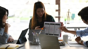 Beautiful woman working as Ux Ui development while showing her project to colleagues at the modern meeting table with office equipment putting on it.