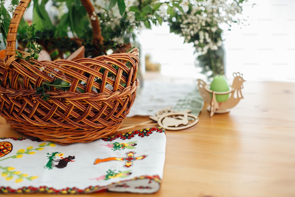 Traditional Easter basket with food for blessing in church and traditional ukrainian embroidery towel for covering basket on wooden table with candle and green boxwood branches and flowers