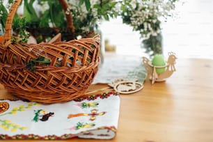 Traditional Easter basket with food for blessing in church and traditional ukrainian embroidery towel for covering basket on wooden table with candle and green boxwood branches and flowers