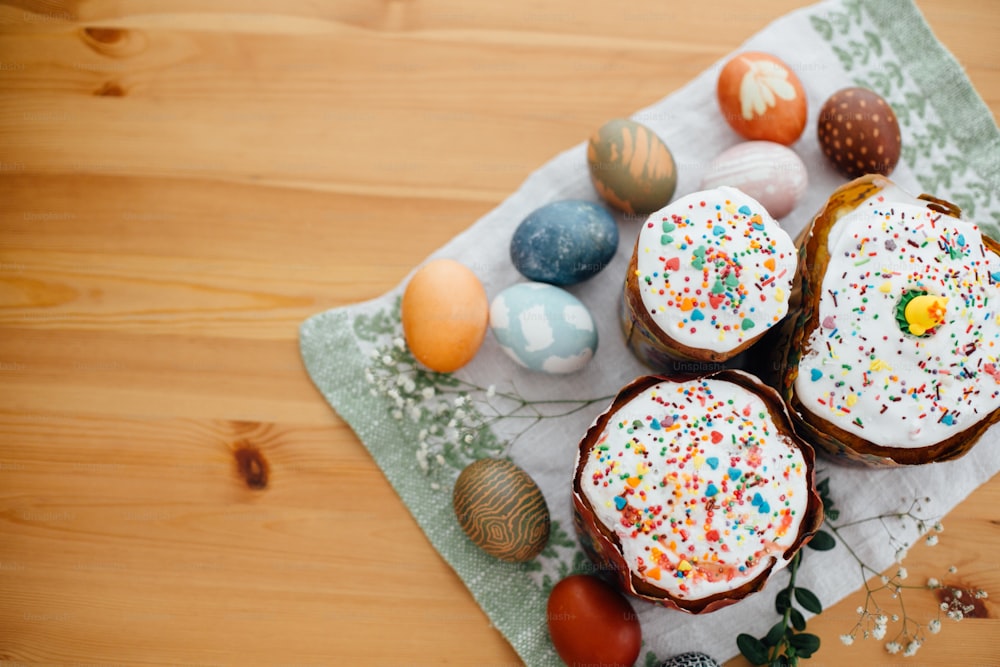 Homemade easter cake and stylish easter eggs natural dyed on rustic cloth with flowers and green brunches on wooden table. Happy Easter. Traditional Easter bread. Flat lay