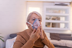 病気の高齢女性が吸入をすると、薬は最高の薬です。酸素マスクを着用し、治療を受けている病気の高齢女性。吸入器を持った年配の女性