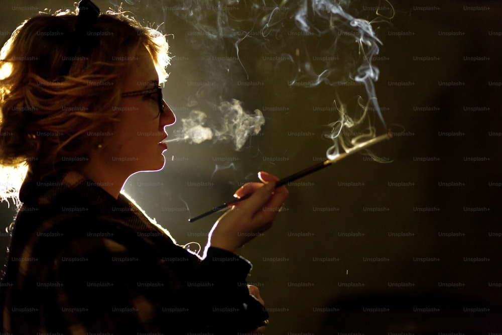 Femme sexy élégante tenant une cigarette et fumant à l’extérieur, visage en gros plan, portrait de femme mystérieuse en manteau vintage, atmosphère noire française, concept de détective