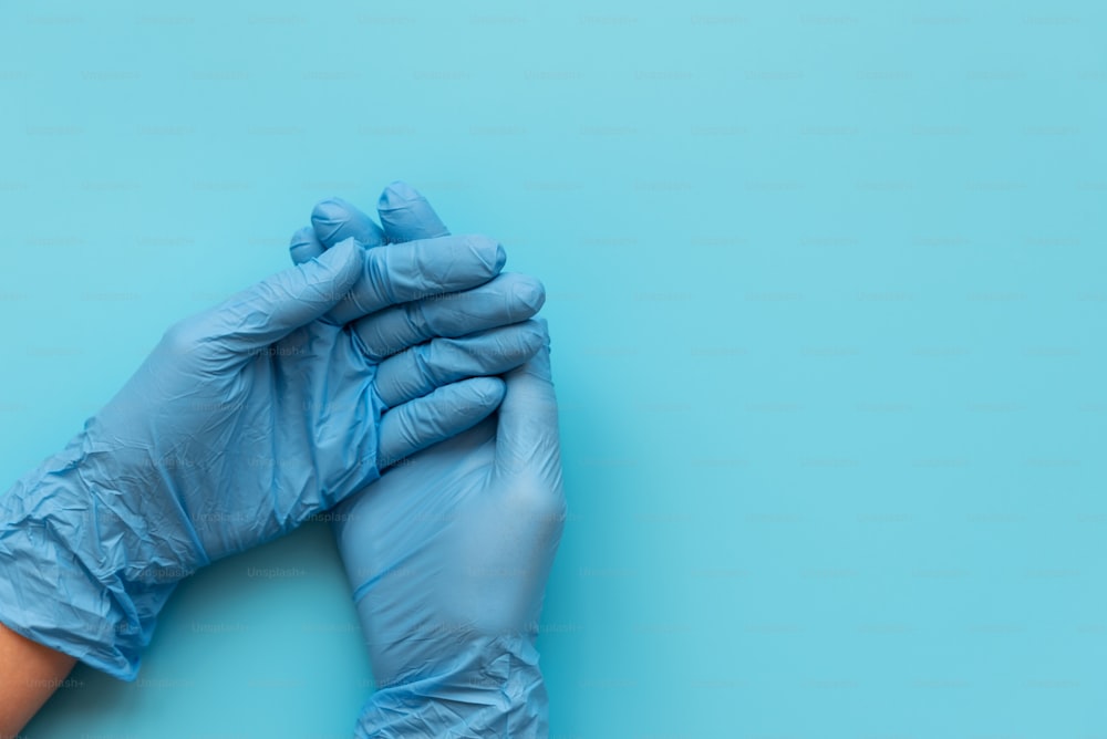 Mani del medico che indossa guanti in lattice blu su sfondo blu. Concetto di protezione