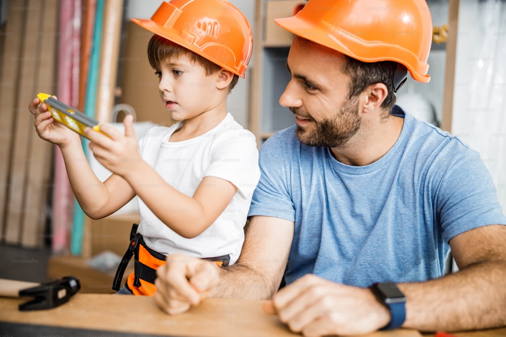 El padre alegre está trabajando y enseñando a su hijo mientras usa instrumentos de mano y cascos. Concepto de familia