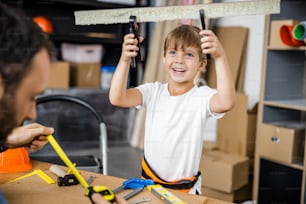 Jolly kid is holding cut desk with pliers after making it together with his dad