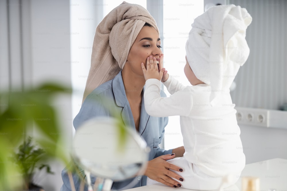 Happy young woman and her kid in towels on their heads and pajamas in the bedroom stock photo